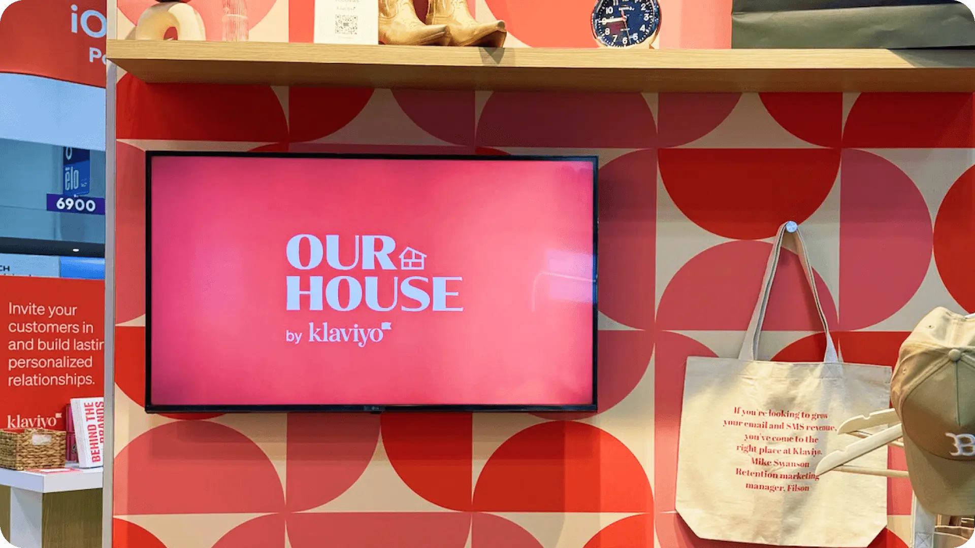 Display with "OUR HOUSE by Klaviyo" text, surrounded by promotional materials and a tote bag with marketing text.