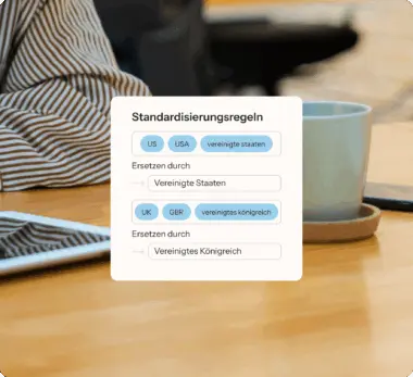 Standardisierungsregeln auf einem Bildschirm, daneben eine Person in gestreiftem Hemd, ein Tablet und eine Tasse auf einem Tisch.