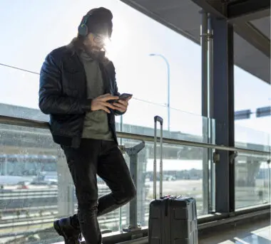 Man at a transit station wearing headphones, looking at his phone.
