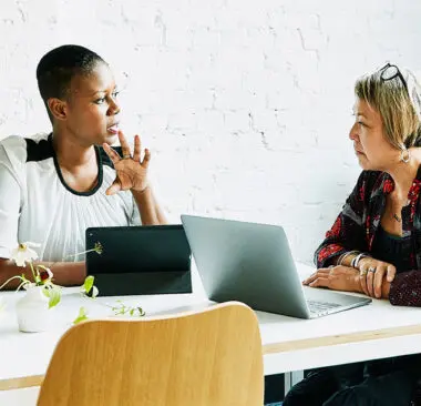 two women talking over a computer and tablet