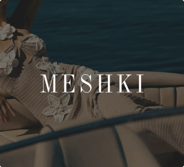 Person in a crochet outfit with floral details lounging on a boat. The text "MESHKI" is overlaid on the image.