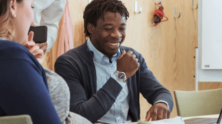 Woman and man sitting at a table, looking down and laughing