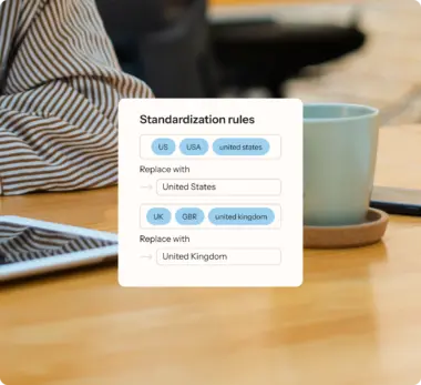 UI card overlaying a workspace image, displaying standardization rules for country names, mapping "US, USA" to "United States" and "UK, GBR" to "United Kingdom."