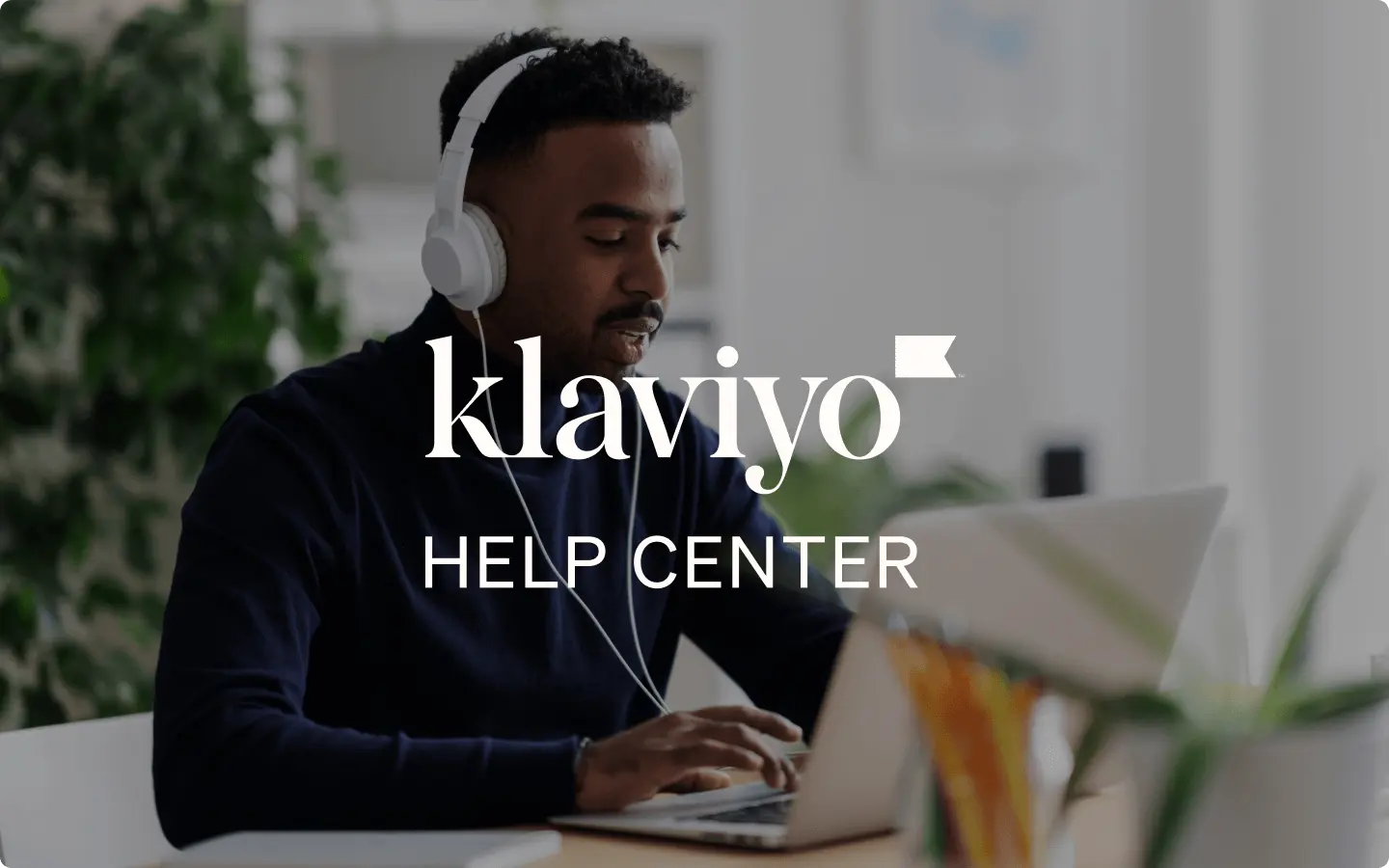 Man wearing white headphones at his desk while joining a call on his laptop, with Klaviyo Help Center text overlay